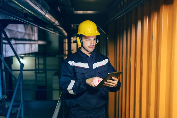 Portrait of young Caucasian man dressed in work wear using tablet while standing in heating plant. - Φωτογραφία, εικόνα