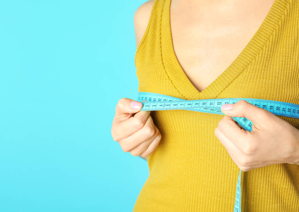 Young woman measuring breast size on color background, closeup view with space for text. Cosmetic surgery - Foto, imagen