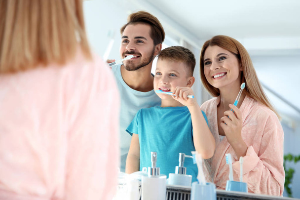 Happy family with toothbrushes near mirror in bathroom. Personal hygiene - Фото, зображення