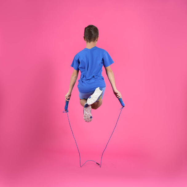 Active boy jumping rope on color background - Фото, изображение