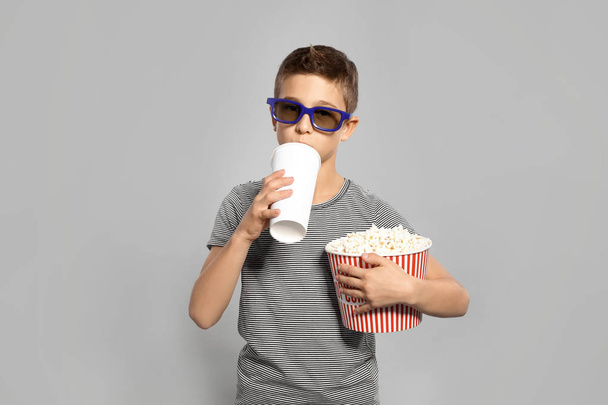 Boy with 3D glasses, popcorn and beverage during cinema show on grey background - Photo, image