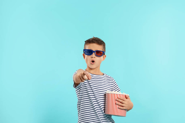 Emotional boy with 3D glasses and popcorn during cinema show on color background - Фото, зображення