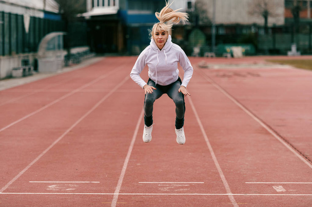 Спортивна розкішна серйозна жінка стрибає на біговій доріжці. Повна довжина, зовнішній вигляд стадіону
. - Фото, зображення