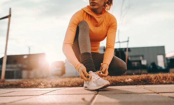 Крупним планом жінка бігунка на колінах і зав'язування шнурки на вулиці в сонячний день
. - Фото, зображення