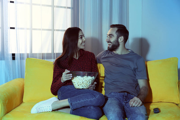 Happy young couple watching TV on sofa at home - Foto, Imagen