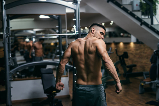 Caucasian muscular shirtless man posing in the gym. Backs turned. - Photo, image