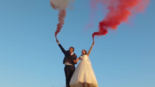 Gelukkige bruid en bruidegom zwaaien gekleurde roze rook tegen de blauwe lucht en lachen. Huwelijksreis. Romantiek. Relatie tussen man en vrouw - Video