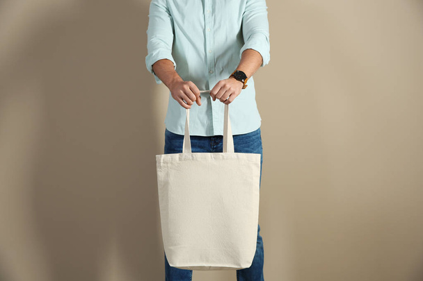 Young man holding textile bag on color background, closeup. Mockup for design - Photo, image