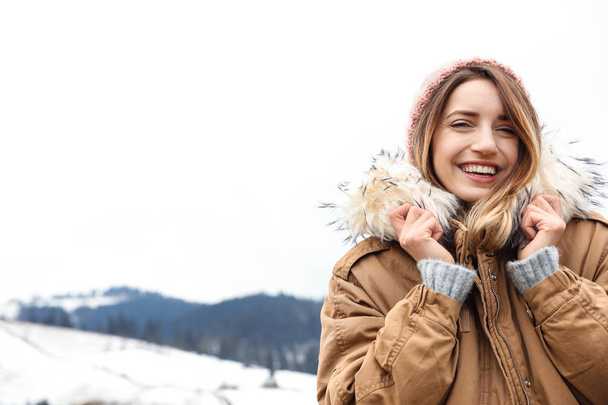Young woman in warm clothes near snowy hill, space for text. Winter vacation - Foto, imagen