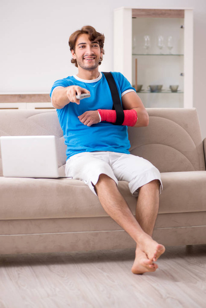 Νεαρός άνδρας με βραχίονα τραυματίες που κάθεται στον καναπέ  - Φωτογραφία, εικόνα