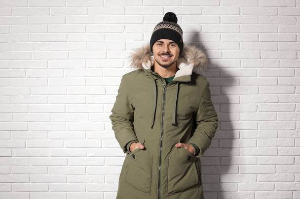 Young man wearing warm clothes against brick wall. Ready for winter vacation - Foto, imagen