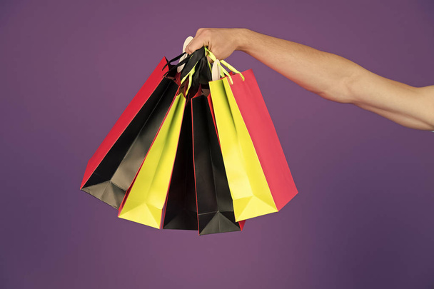 Shopping bags in hand on violet background. Paper bags of different colors. Bags or paperbags. Shopping or sale and black friday concept. Holidays preparation and celebration. Gift and present - Zdjęcie, obraz