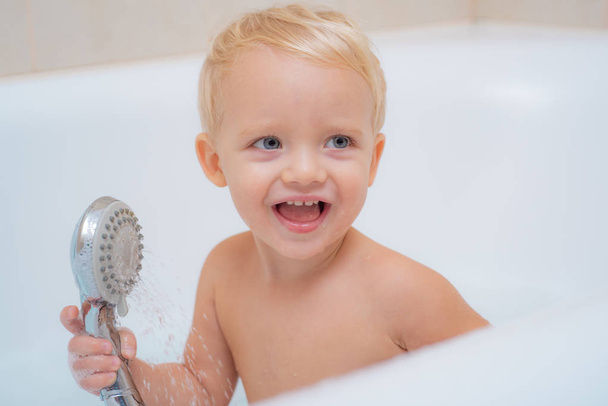 Child bubble bath. Pretty smiling little boy taking a bath with soap suds. Cute little boy washing. Kid in bath. - Fotó, kép