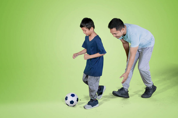 Image of little boy and his father playing football in the studio with green screen - Valokuva, kuva