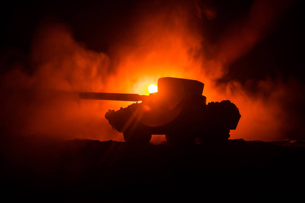 Concepto de guerra. Silueta de tanque blindado Debajo del cielo de fuego de niebla por la noche. Escena de ataque. Decoración de juguete. Enfoque selectivo
 - Foto, Imagen