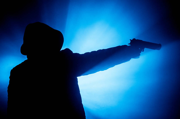 Σιλουέτα του ανθρώπου με πιστόλι έτοιμοι να επιτεθούν στο σκοτάδι τονισμένο ομιχλώδες φόντο ή επικίνδυνο ληστή εκμετάλλευση όπλο στο χέρι. Γυρίσματα τρομοκράτης με το όπλο θέμα ντεκόρ - Φωτογραφία, εικόνα