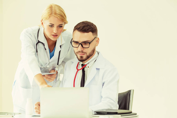 Médecin au bureau de l'hôpital travaillant sur ordinateur portable sur la table avec un autre médecin ayant une discussion sur la santé des patients
. - Photo, image