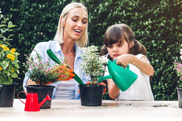 Mutter mit kleiner Tochter hat Spaß und pflanzt gemeinsam Blumen in Topf mit Erde, Tochter kümmert sich um Blumen mit Bewässerungspflanzen im Garten zu Hause - Foto, Bild