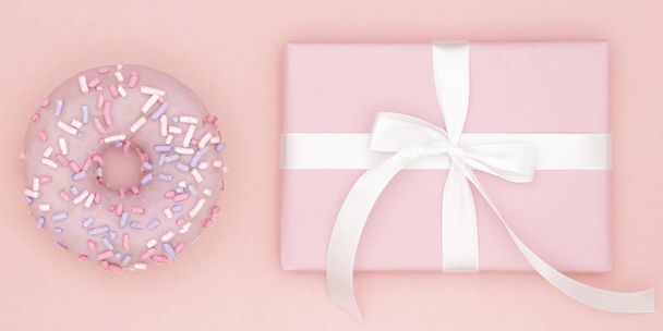 Valentinstag oder Geburtstag Draufsicht Zusammensetzung rosa Geschenk mit weißem Band mit süßem Donut auf Korallenpapier Hintergrund. Konzept Dekor Love Day oder Frauentag. flache Lage - Foto, Bild