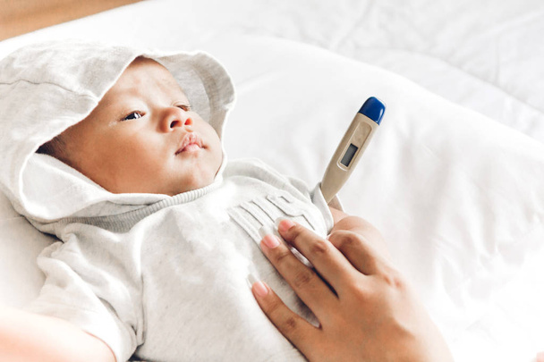 Mãe segurando termômetro de seu bebê doente.Bebê doente na cama com febre medição de temperatura
 - Foto, Imagem