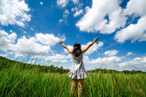 Young beautiful woman on green grass meadow spreading arms to the blue sunny sky on summer day. Getaway and meditation concept. - Photo, Image