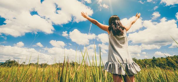 Joven mujer hermosa en el prado de hierba verde extendiendo los brazos al cielo azul soleado en el día de verano. Escapada y concepto de meditación
. - Foto, imagen