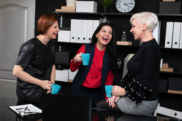 Tre donne d'affari che parlano con il caffè in mano in ufficio alla moda
 - Foto, immagini
