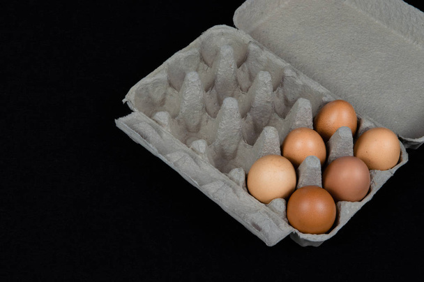 Sei uova di pollo in una scatola di cartone, isolate su fondo di feltro nero
. - Foto, immagini