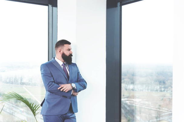 Serious concerned leader with beard standing by window in office - Foto, Bild