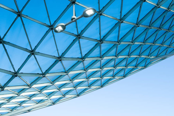 Moderní architektura prosklená střecha s prohnutým designem ocelové konstrukce. Nízký úhel pohledu s modrou oblohou, vnitřní osvětlení a bílé zdi budovy - Fotografie, Obrázek