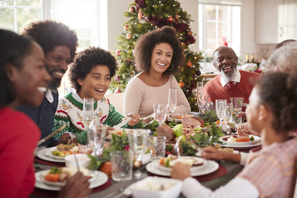 Happy-multi generation mixed race family sitting at their Christmas dinner table eating and talking, selective focus - 写真・画像
