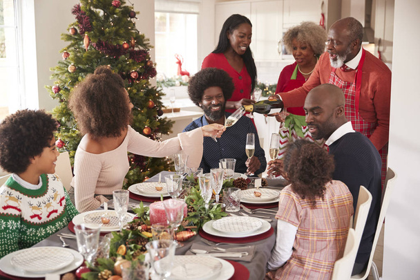 Grandfather pouring champagne at the dinner table during a multi-generation, mixed race family Christmas celebration - 写真・画像