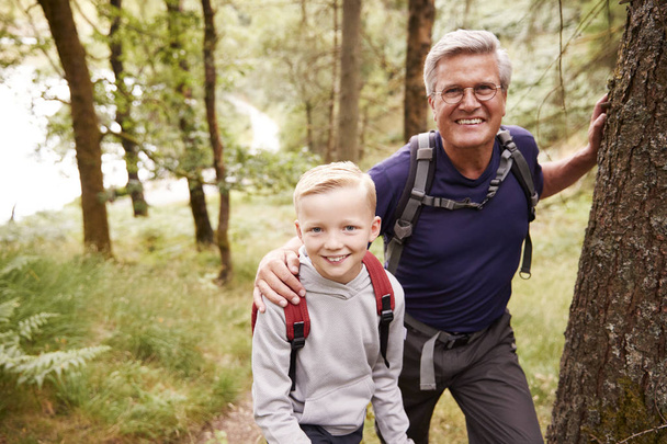 Grandfather and grandson taking a break while hiking together in a forest, close up, smiling to camera - Фото, зображення