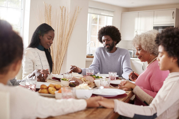 Multi-generation mixed race family holding hands and saying grace before eating their Sunday dinner - Photo, Image