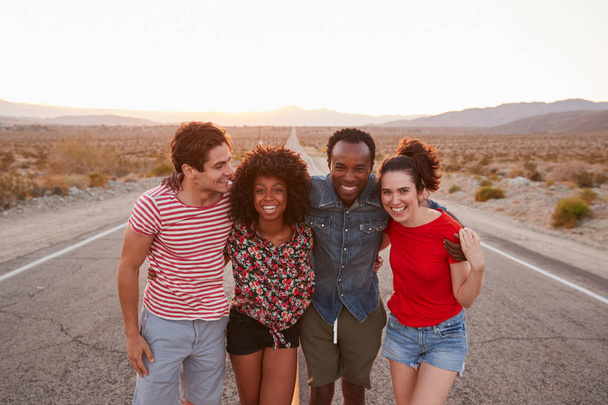 Four happy friends standing on a desert highway - Photo, image