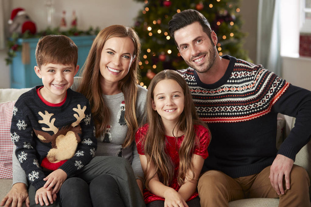 Portrait Of Parents With Children Wearing Festive Jumpers Sitting On Sofa In Lounge At Home On Christmas Day - Valokuva, kuva