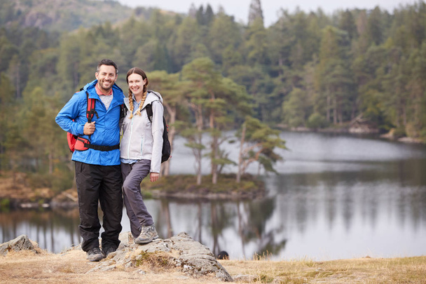 Young adult couple standing on a rock beside a lake in countryside, smiling to camera, full length - Foto, Imagem