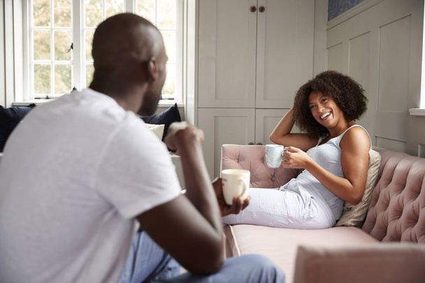 Young adult black woman sitting on a couch with coffee smiling at her partner - Foto, Bild