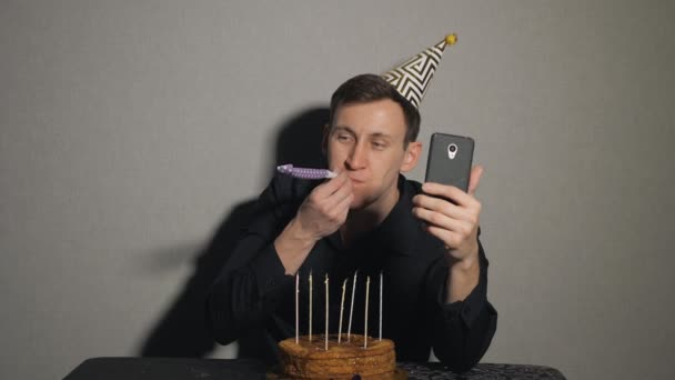 mladý muž s čokoládový dort a svíčky s party dmychadla a bere selfie - Záběry, video
