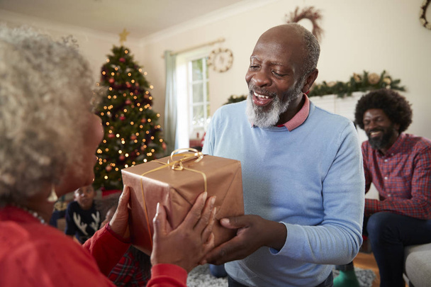 Senior Couple Exchanging Gifts As They Celebrating Christmas At Home With Family - Photo, Image