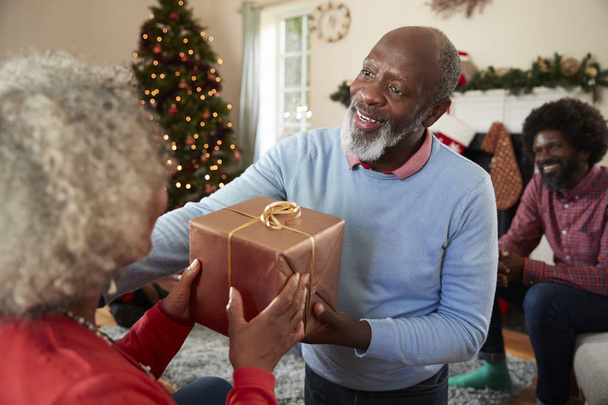 Senior Couple Exchanging Gifts As They Celebrating Christmas At Home With Family - Foto, imagen
