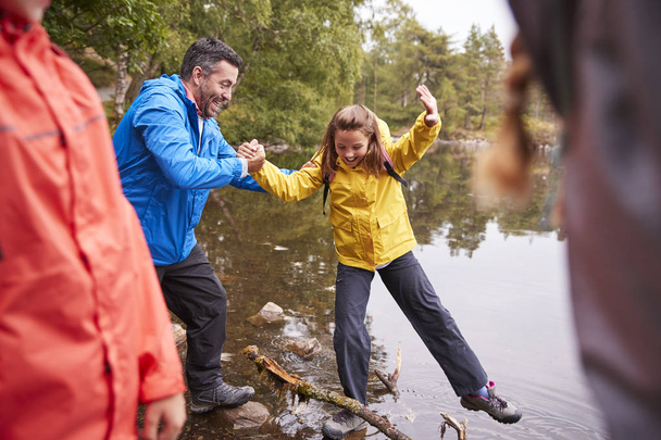 Middle aged father holding his daughters hand while she balancing on the shore of a lake - Photo, Image
