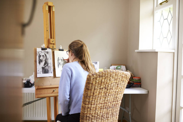 Vista trasera de la artista adolescente sentada en el caballete dibujando el cuadro del perro desde la fotografía en carbón
 - Foto, imagen