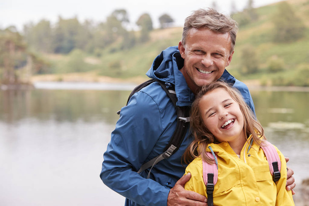 Caucasian pre-teen girl standing with her father on the shore of a lake, laughing at camera - Фото, зображення