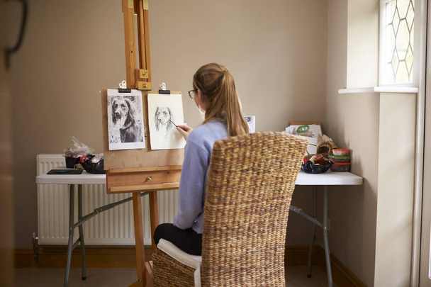Vista lateral do artista adolescente feminino sentado no cavalete desenho imagem do cão da fotografia em carvão vegetal
 - Foto, Imagem