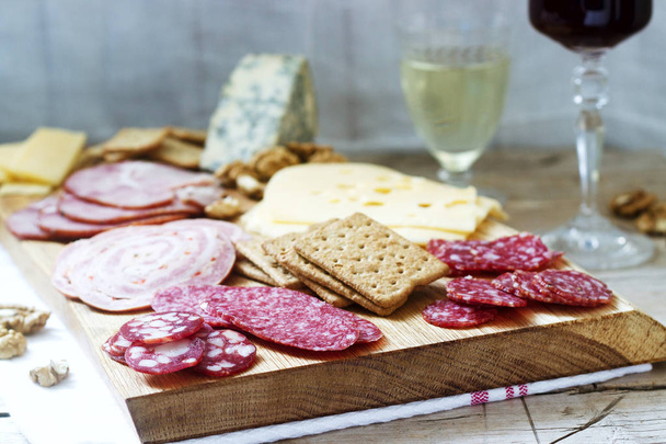 Aperitivo de vários tipos de salsichas, carnes, queijos e biscoitos em uma tábua de madeira, servido ao vinho
. - Foto, Imagem