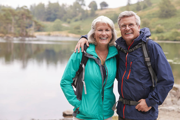 Happy senior couple standing on the shore of a lake smiling to camera, Lake District, UK - Photo, image