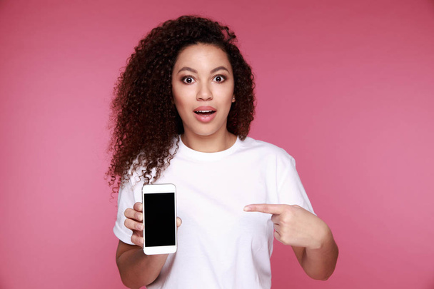 Portrait of a shocked young african woman talking on mobile phone and looking away isolated over pink background - Photo, image