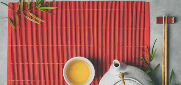 tea set and chopsticks on red bamboo mat on gray stone background - Fotó, kép
