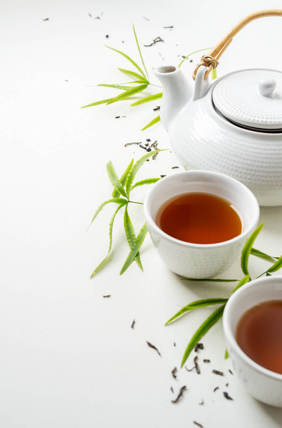 Азиатский набор с зеленым чаем, чашки и чайник на белом фоне с зелеными листьями
  - Фото, изображение